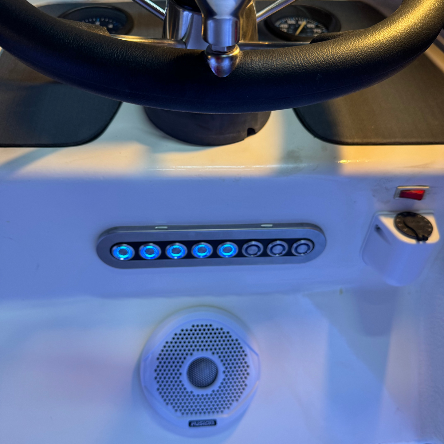 A custom switch panel with blue back-lit push switches installed in a vehicle interior setting, likely a boat due to the marine backing rubber.