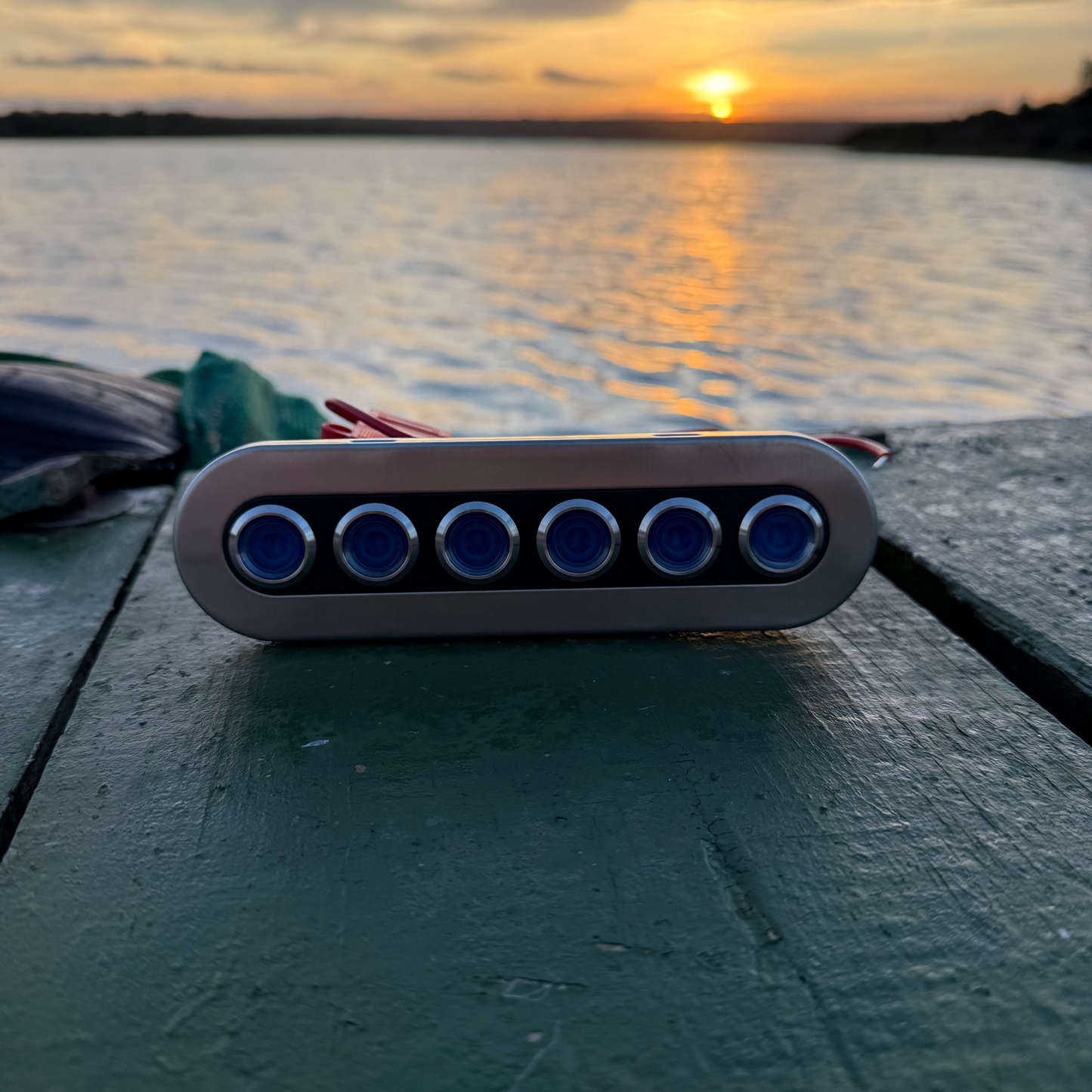 Electronic device with blue lights on a wooden surface during sunset over water