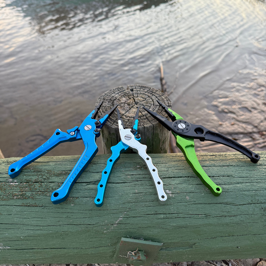 Three pliers in blue, white, and green on a wooden post by a body of water.