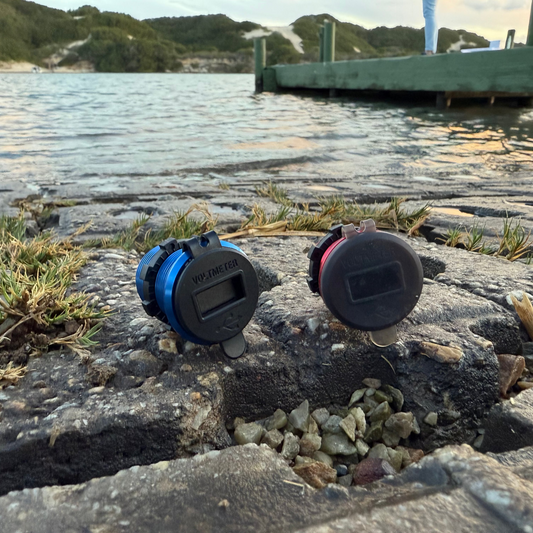Two small electronic devices on a stone surface near water with a dock in the background.