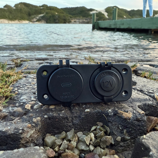 Black dual socket on a rocky surface with water and a dock in the background