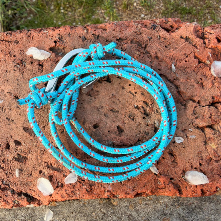A coiled turquoise blue rope with small orange and white speckles, tied with a knot and secured with a metal clip, placed on a textured reddish-brown stone surface outdoors.