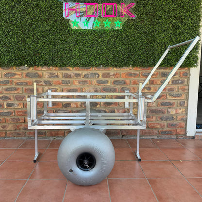 Metal bench and gray spherical object on a tiled patio with a brick wall and greenery in the background.