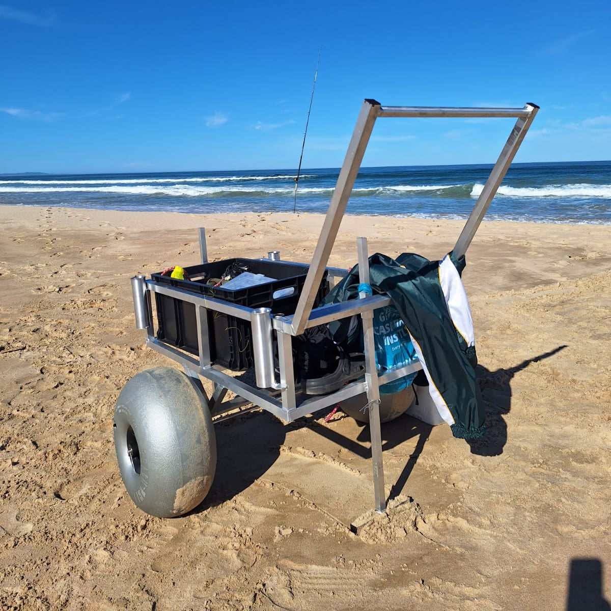 2 wheel beach trolley loaded on a sandy beach with a fishing rod in the background