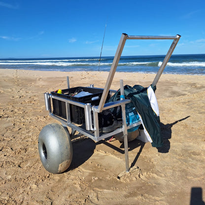 2 wheel beach trolley loaded on a sandy beach with a fishing rod in the background