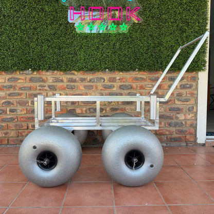 Metal cart with large wheels on a tiled patio, against a brick wall with greenery.