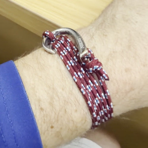 A close-up of a person's wrist wearing a maroon and white braided cord bracelet with a silver metal ring clasp.