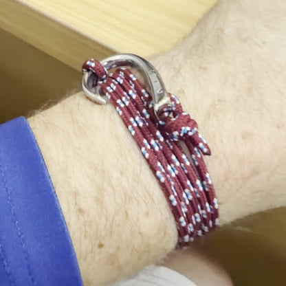 A close-up of a person's wrist wearing a maroon and white braided cord bracelet with a silver metal ring clasp.