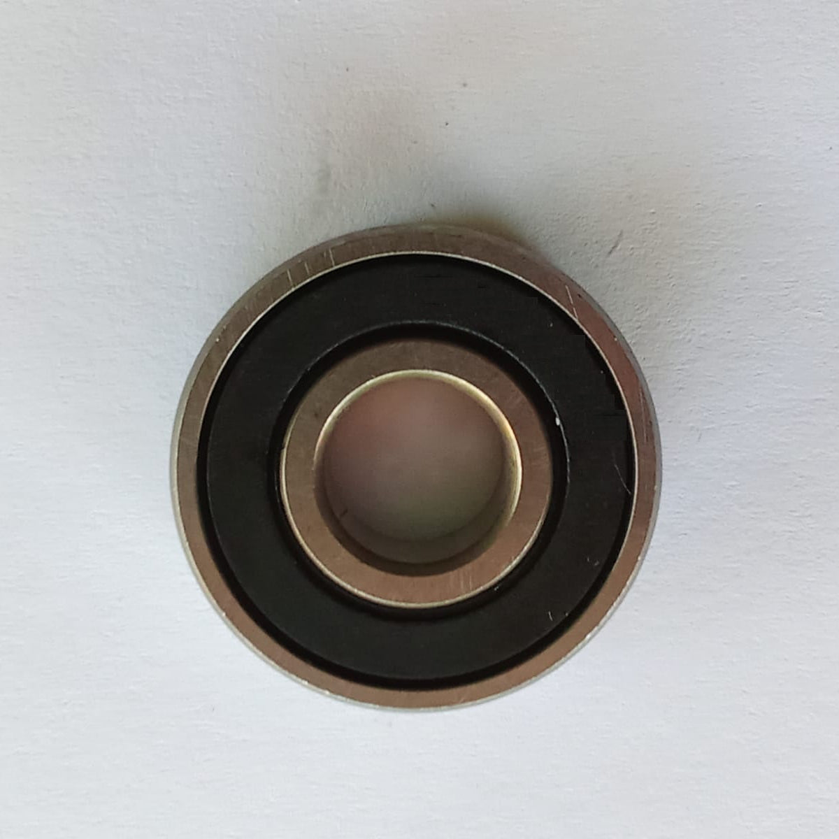 A close-up of a metal bearing component with a black inner ring and a gold-toned outer ring, photographed on a plain white surface.
