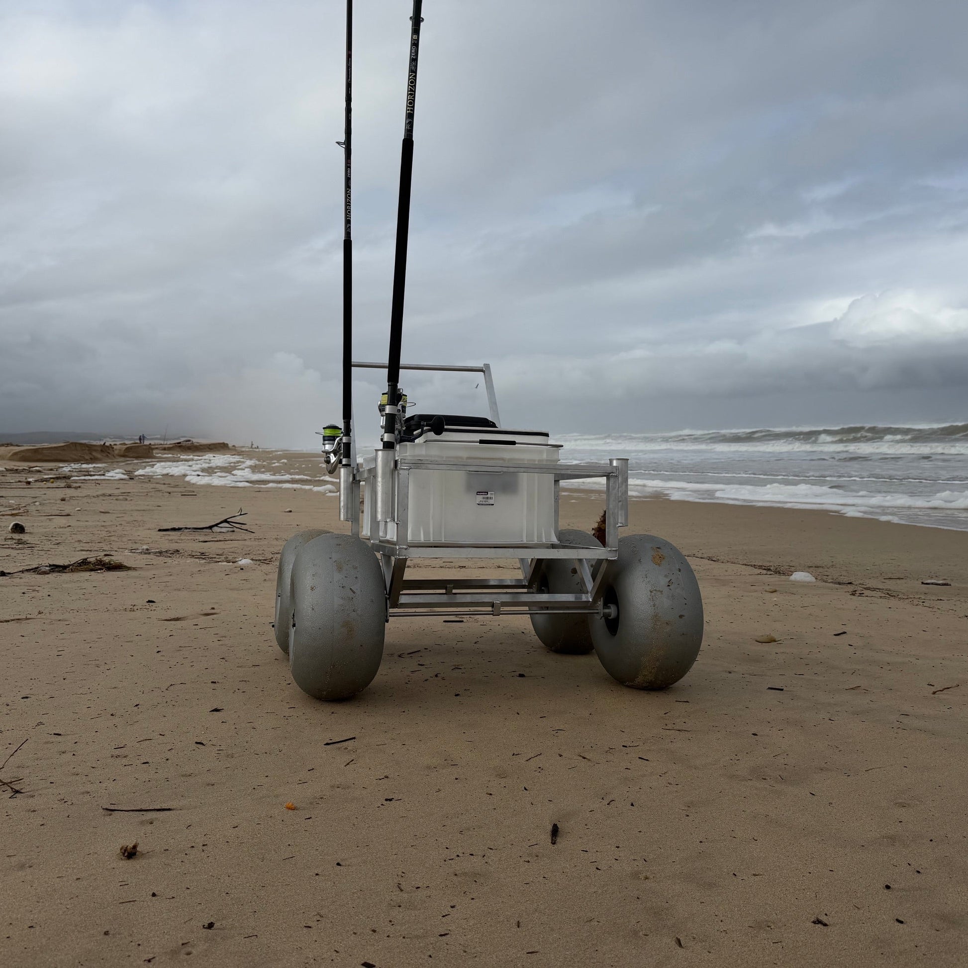 Front view of Tidal Hook beach fishing cart with oversized balloon wheels, rod holders, and storage crate designed for easy transport of surf fishing gear.