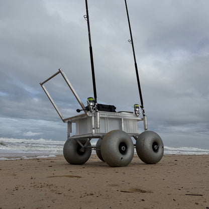 Beach fishing cart with oversized balloon wheels, dual rod holders and storage crate shown on soft sand for easy transport of surf fishing gear.