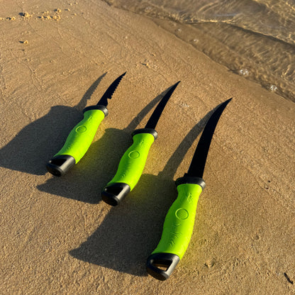 Three black fillet knives with bright green handles displayed on a sandy beach, showcasing different blade styles for fish cleaning and filleting.